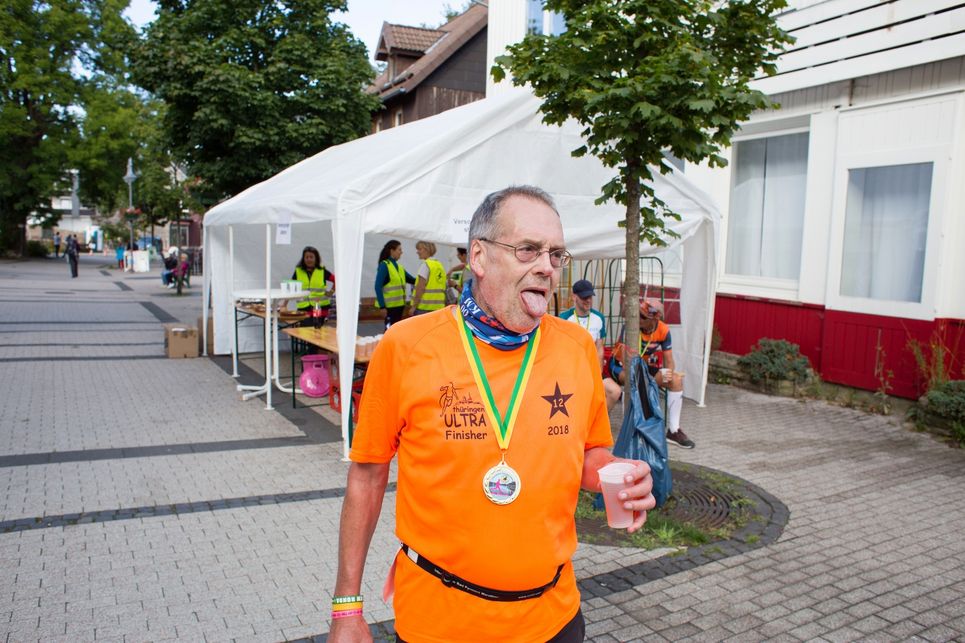 Hans G. Drexler streckt erschöpft die Zunge heraus, ein Getränk in der Hand.