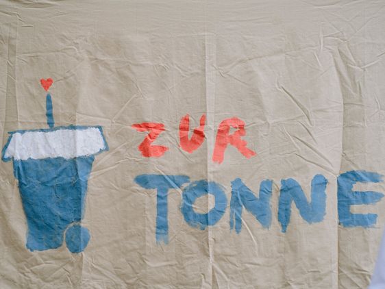 Stoff mit der Aufschrift "Zur Tonne" und einer gezeichneten Mülltonne mit Strohhalm.