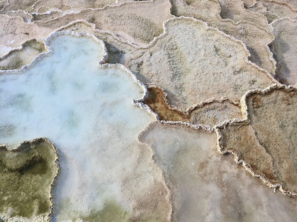 Salzverkrustete Oberfläche, hellblaues, dampfendes Wasser.