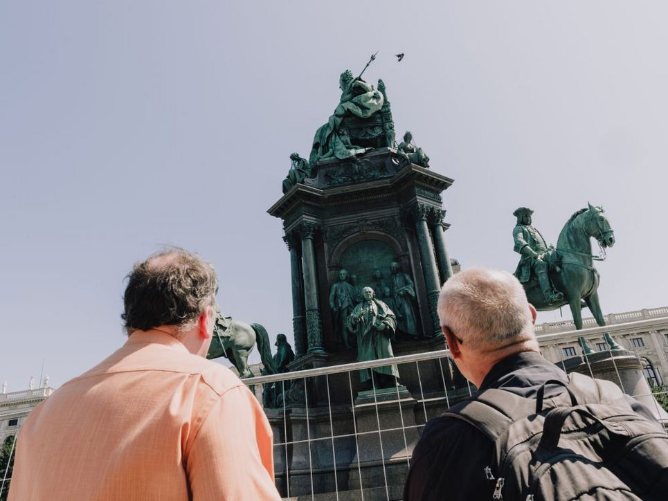 Zwei Personen von hinten, Blick auf ein monumentales Reiterdenkmal. Dahinter ist der blaue Himmel zu sehen.