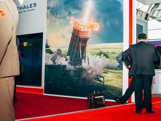 Zwei Herren in Anzügen, einer in Uniform for einem Plakat einer Raketenabwehr-Maschine.zu sehen und einer in Uniform, der ebenfalls nur halb zu sehen ist, von  
