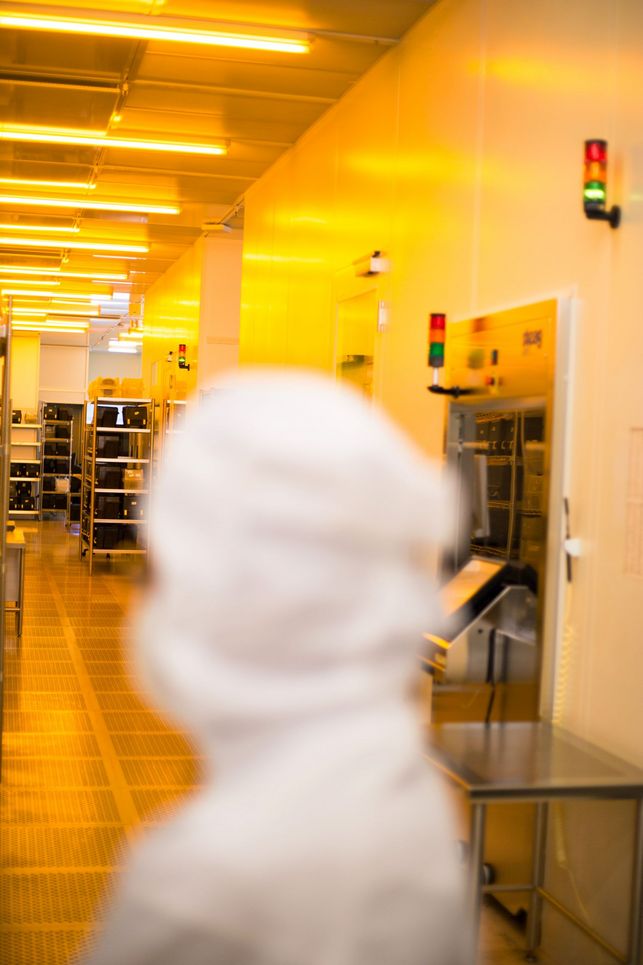 Person in weißem Schutzanzug im Reinraum, der in gelbliches Licht getaucht ist.