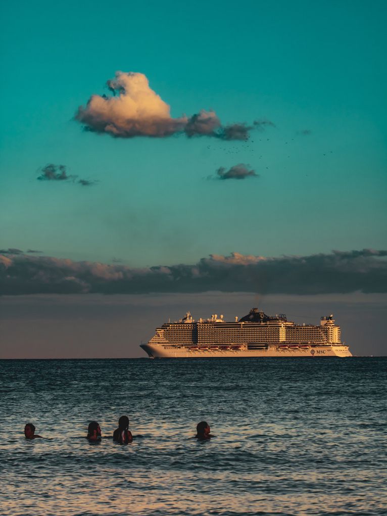 Badende mit Blick auf ein Kreuzfahrtschiff.