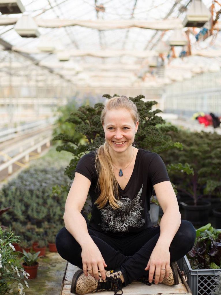 FRANZISKA HANSCHEN im Schneidersitz vor einem großen Grünkohl im Gewächshaus.