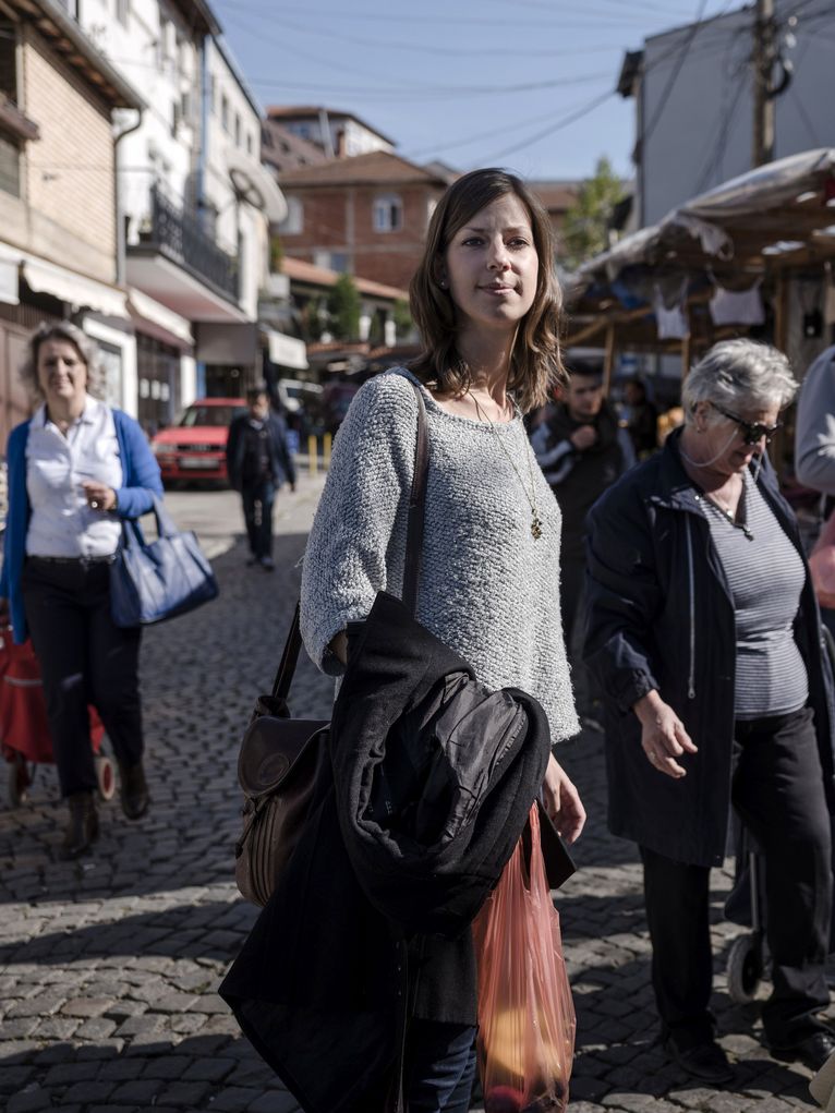 Janine Läpple mit mit Jacke, Umhängetasche und Einkaufstüte auf einem Markt