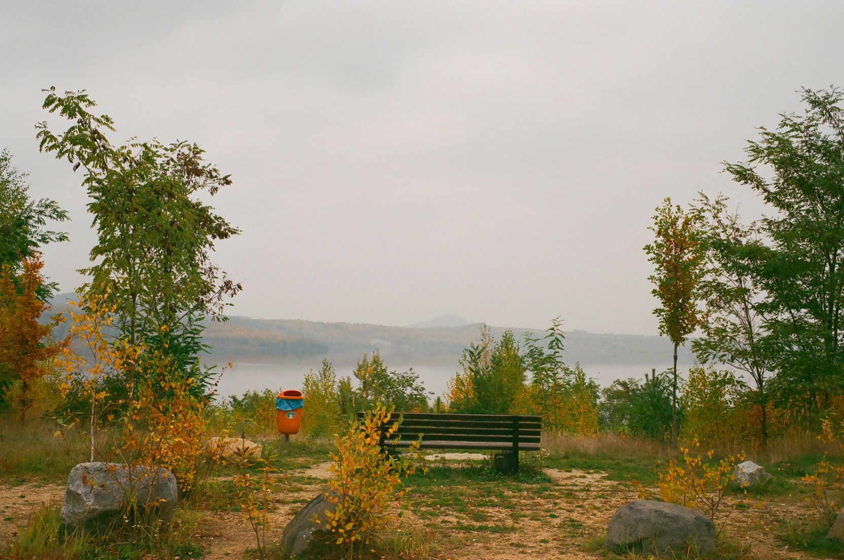 Bank und Mülleimer, Blick auf den Bergdörfer See und dahinterliegende Berge.