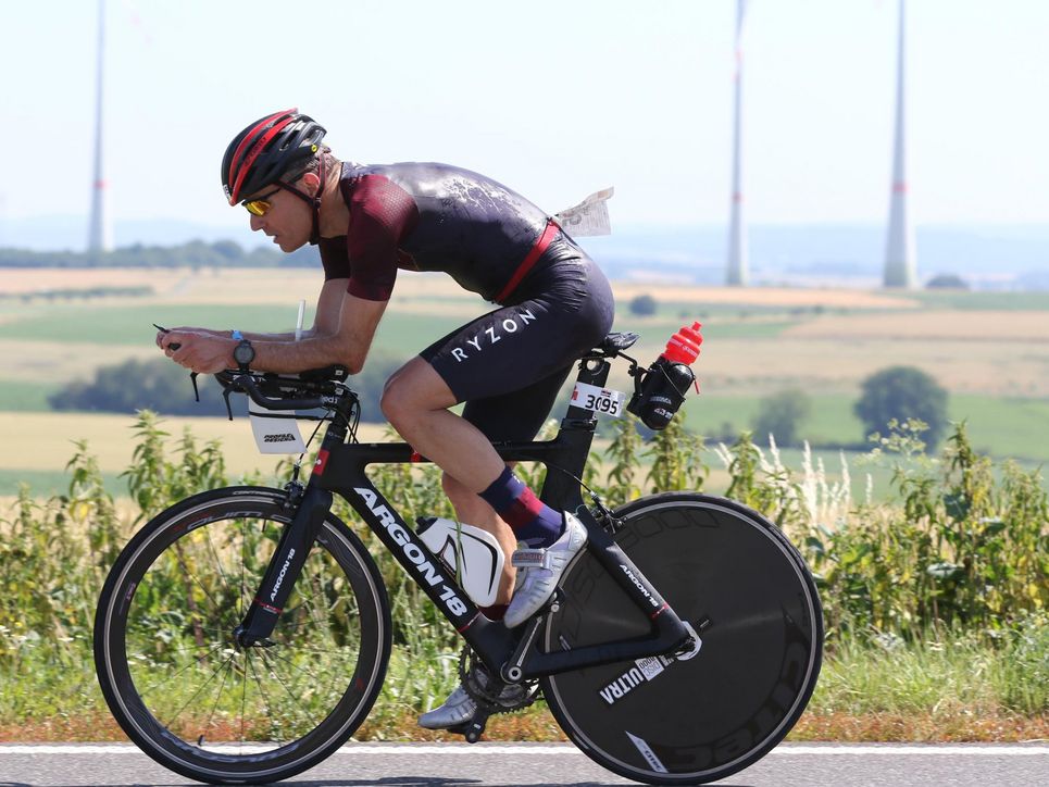 Christoph Englert auf einem Rennrad, hinter ihm Felder und Windräder.