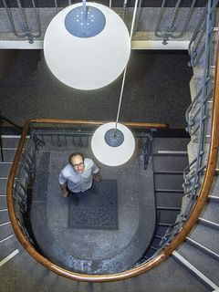 Robert Luther steht im Treppenhaus des MfN, sein Blick folgt den Lampen, die wie Planeten von der Decke schweben.