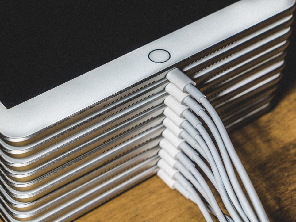 Übereinandergestapelte weiße iPads, die alle mit einem Ladekabel verbunden sind