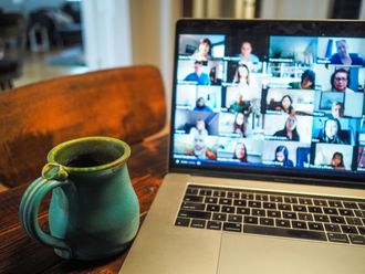 Auf einem Tisch steht eine Tasse und ein Laptop, über den eine Videokonferenz abgehalten wird.
