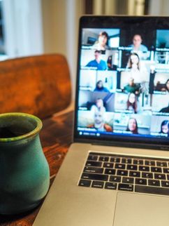 Auf einem Tisch steht eine Tasse und ein Laptop, über den eine Videokonferenz abgehalten wird.