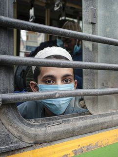 Junge mit OP-Maske schaut aus dem Fenster eines Zuges.