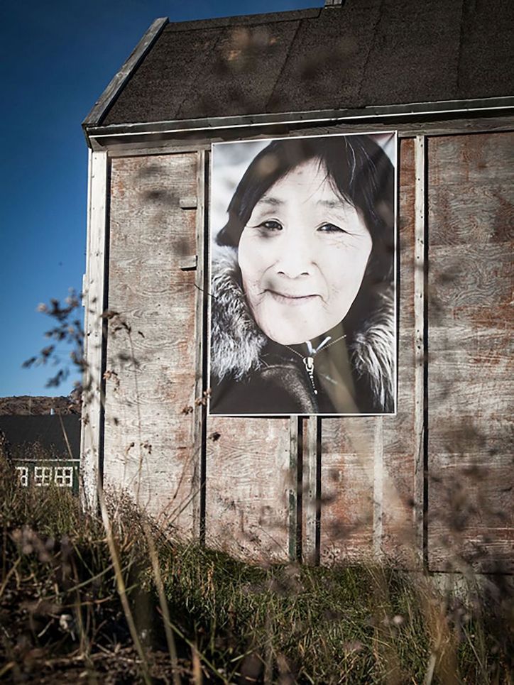 Foto einer älteren Frau an einer Hauswand.