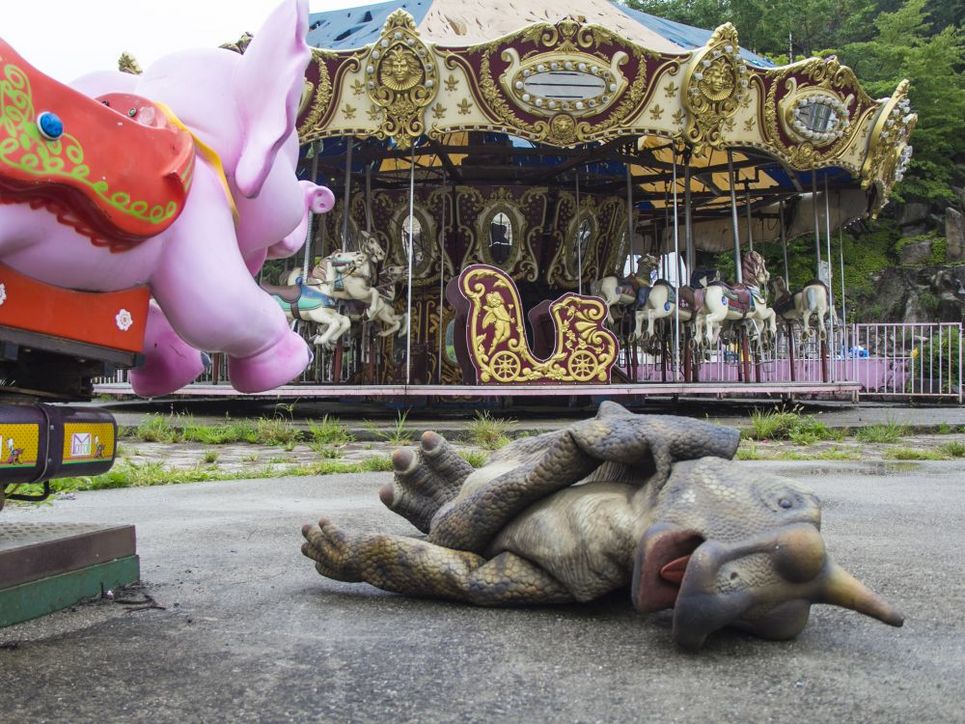 Kirmes mit Karussellen und einem Dinosaurier aus Plastik, der auf dem Boden liegt. 