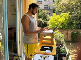 Ilyas Saliba arbeitet stehend am Laptop auf seinem Balkon.