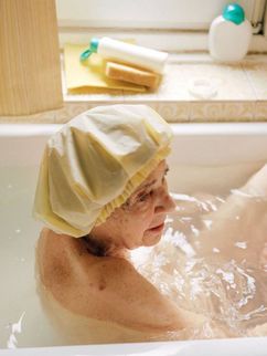 Eine alte Frau mit Badehaube in der Badewanne.