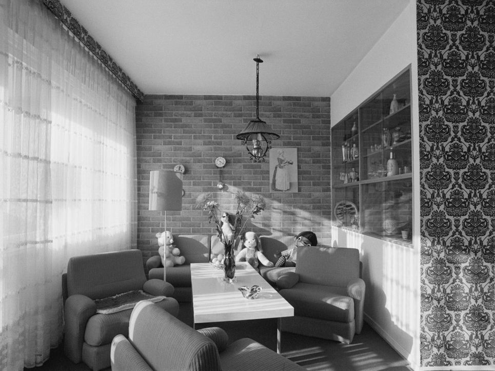 Tisch, verstreut stehende Sessel, Sofa mit Kuscheltieren, Stehlampe im Wohnzimmer des Wohnungstyps P2.