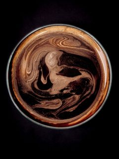 Draufsicht auf eine Tasse Kaffee mit schaumiger Oberfläche und braunen Wirbeln.