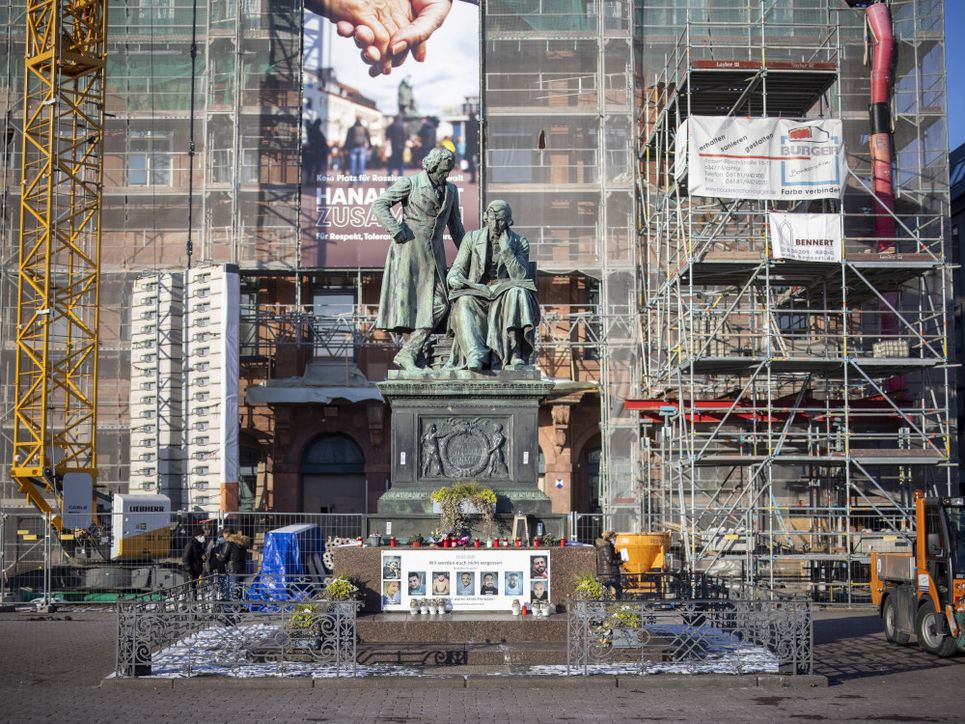 Gedenkkerzen, Fotos, Blumen am Fuße eines Denkmals vor einer Baustelle.