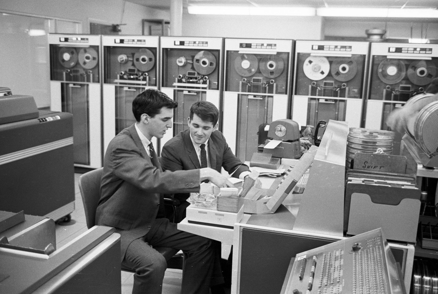 Zwei junge Männer im Anzug in einem Computerraum in den 60er Jahren.