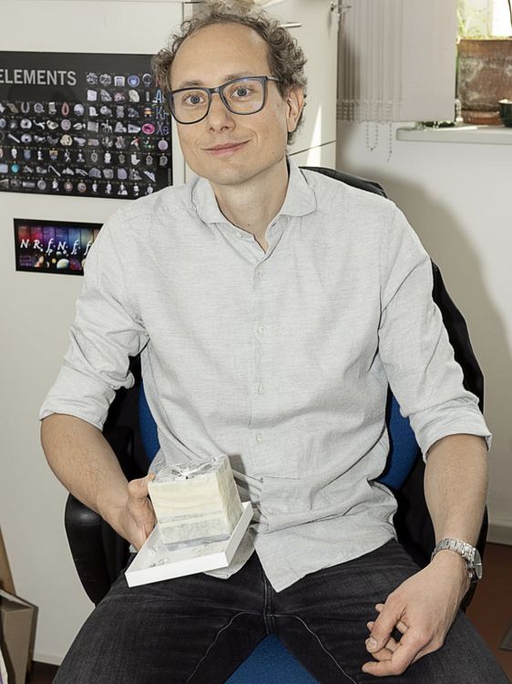 Robert Luther blickt in die Kamera, er hält einen Steinwürfel in der Hand.