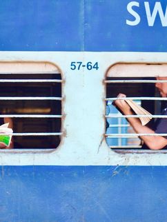 Zwei Lesende sind durch die vergitterten Fenster eines Zuges zu sehen.