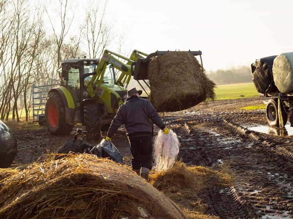 Person bei der Arbeit auf dem Feld mit Traktor, der einen Heuballen aufgespießt hat.