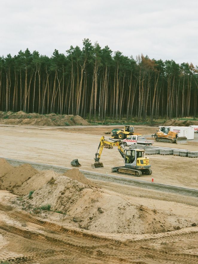 Bagger auf sandiger Baustelle, dahinter Wald.