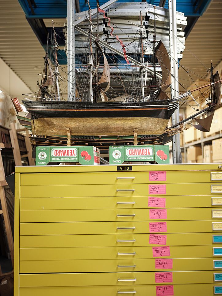 Ein gelber Aktenschrank mit vielen Schubladen und pinken Post-Its, darauf ein Holzmodell eines historischen Segelschiffs