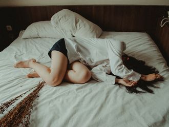 Eine scheinbar unglückliche Frau liegt zusammengekrümmt auf ihrem Bett.
