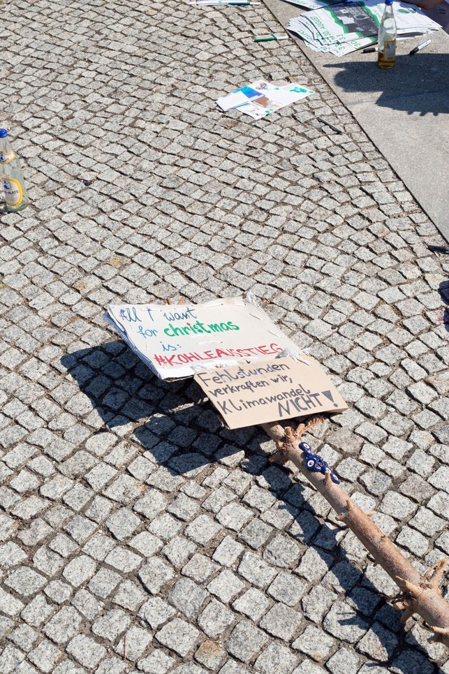 Schild mit der Aufschrift "All I want for Christmas is Kohleausstieg" und "Fehlstunden verkraften wir, Klimawandel nicht" liegt auf dem Bürgersteig.