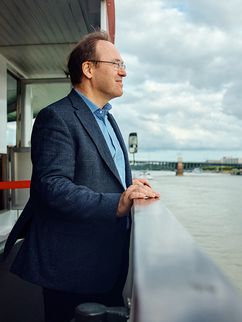 Gewässerökologe Klement Tockner steht an der Reling des Rheindampfers und schaut auf den Fluss.