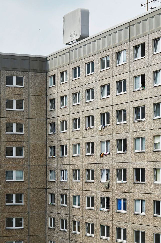 Plattenbau, aus dessen Fenstern zum Teil Wäsche hängt.