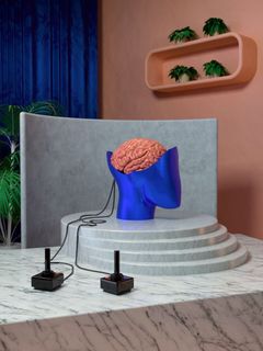 Skulptur eines menschlichen Gehirns, das über Kabel mit zwei Joysticks verbunden ist.