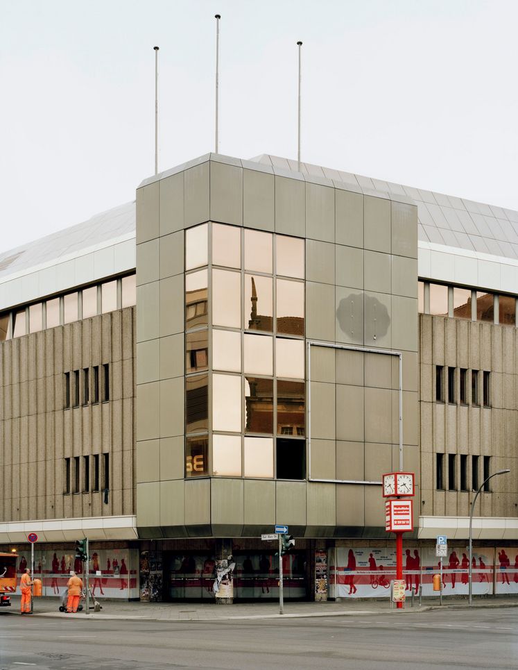 Zum Teil verspiegelte Fassade, davor eine Straßenuhr und Stadtarbeiter.
