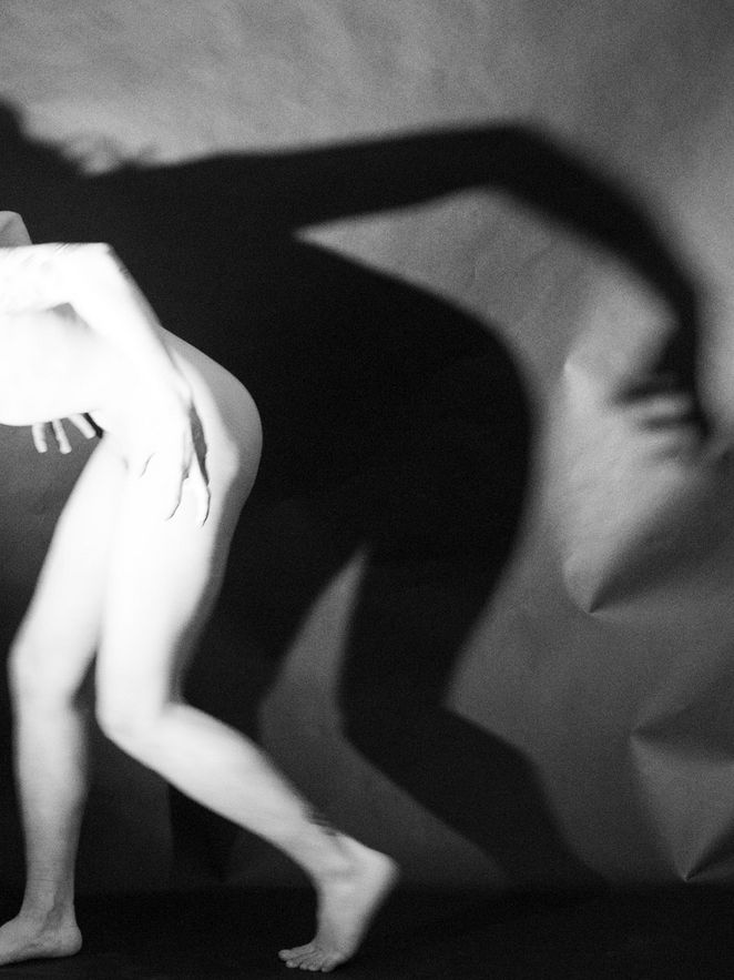 Schwarzweißfotografie eines nackten menschlichen Körpers in Bewegung; der Körper ist teilweise unscharf, dahinter wirft er einen großen, verzerrten Schatten an die Wand.