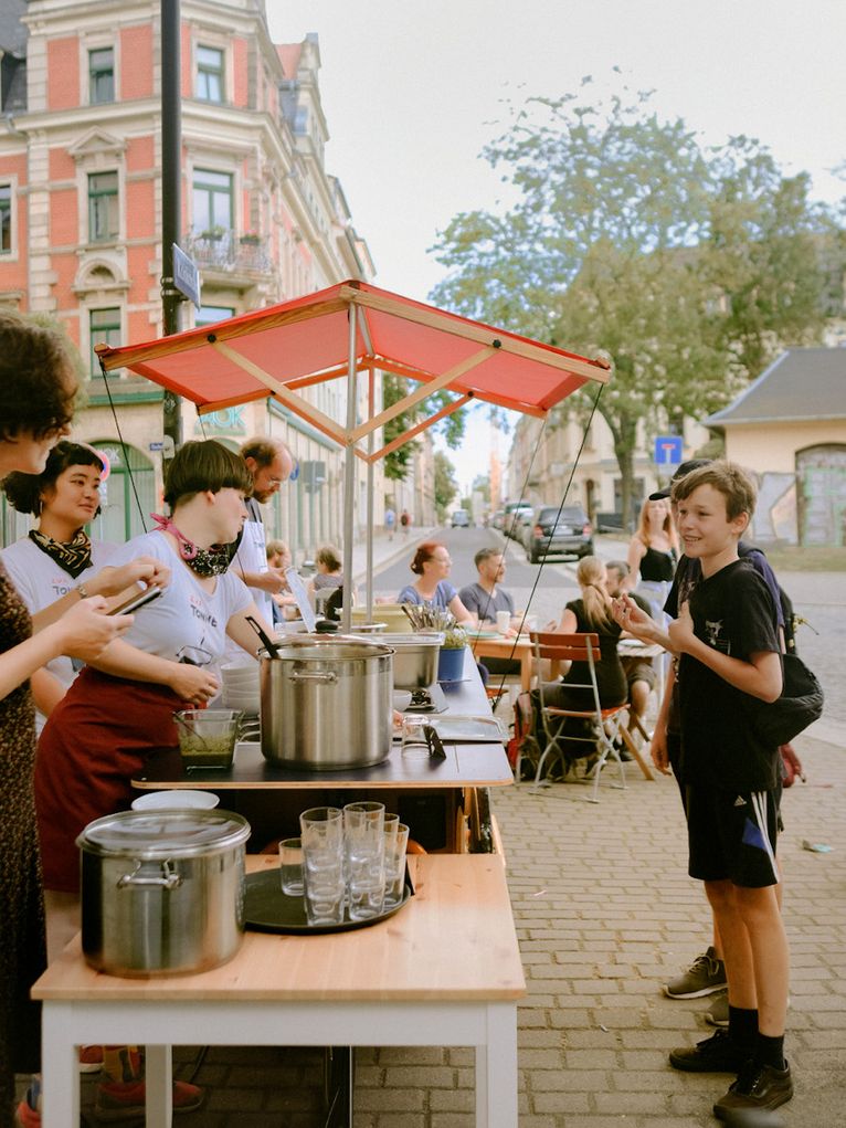 Essensverkauf auf der Straße, zwei Kinder vor dem Stand, Erwachsene dahinter.