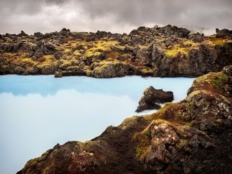 Hellblaues Wasser, umgeben von bräunlichen Felsen.
