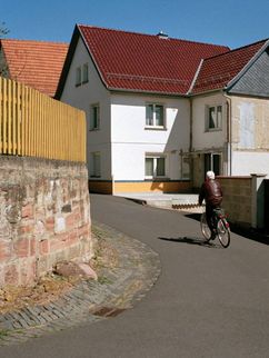 Sonnige Straßenkurve in einem Dorf mit Fahrradfahrer.