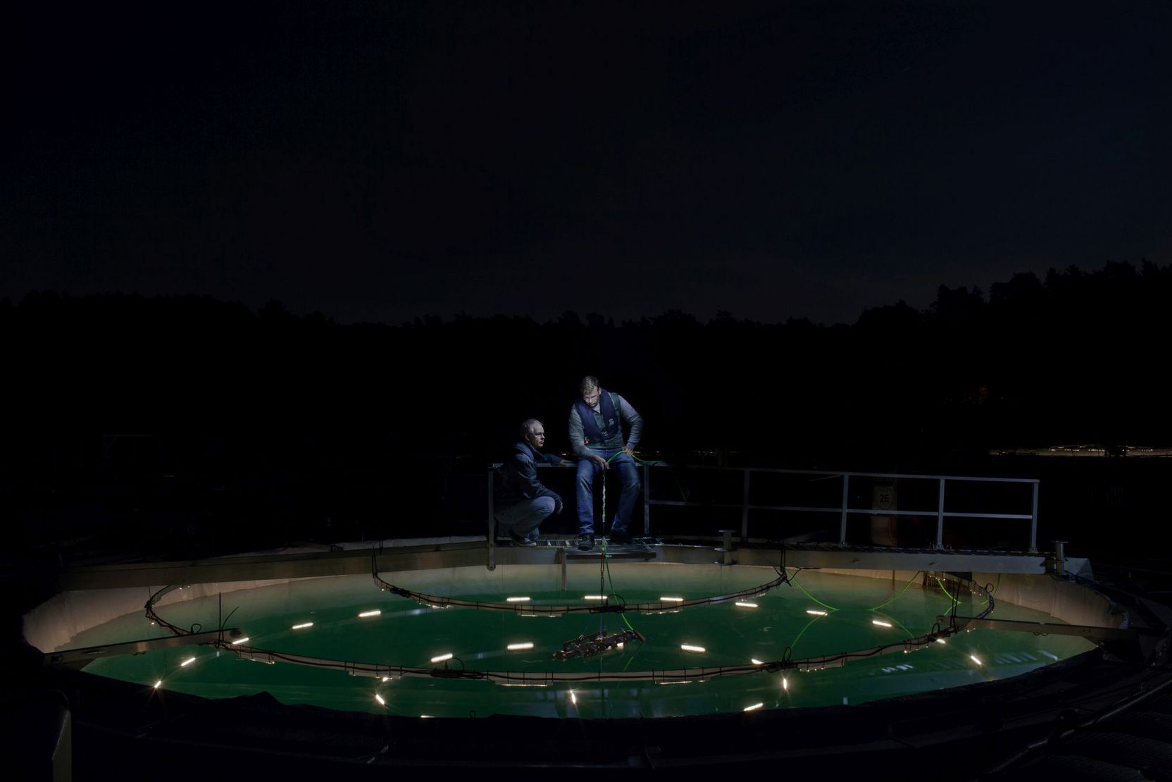 Tim Walles und ein weiterer Wissenschaftler auf einem Steg über einer grünlich schimmernden Wassergrube.