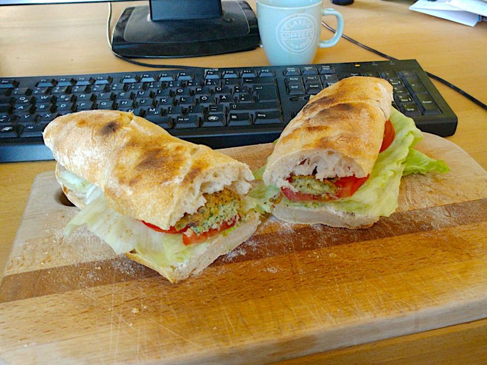 Belegtes Baguette in zwei Hälften auf einem Holzbrett vor Tastatur.