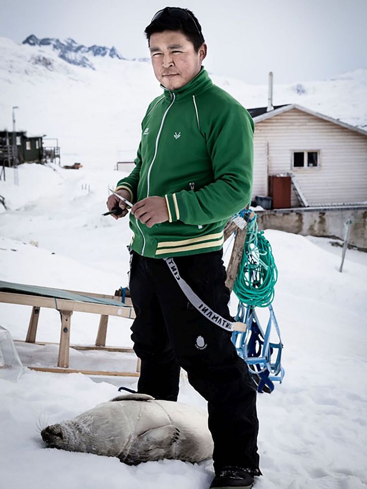 Junger Mann mit einer toten Robbe und einem Schlitten im Schnee.