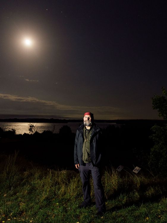 Ralf Koch, Naturparkleiter vom Naturpark Nossentiner/Schwinzer Heide steht und schaut zur Kamera. Hinter ihm ist der Krakower See und der Mond steht hoch am Himmel.