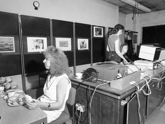 Schwarzweißfotografie von drei Frauen in einem Raum mit alten Computern. Eine von ihnen isst.