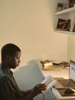 Junger Mann sitzt am Arbeitsplatz mit Buch in den Händen.