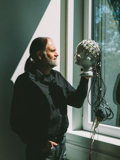 Stephan Getzmann mit Blick aus dem Fenster. Er hält einen verkabelten Puppenkopf in der Hand.
