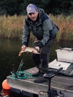 Robert Arlinghaus hält einen gefangenen Fisch auf einem Holzsteg über dem Wasser.