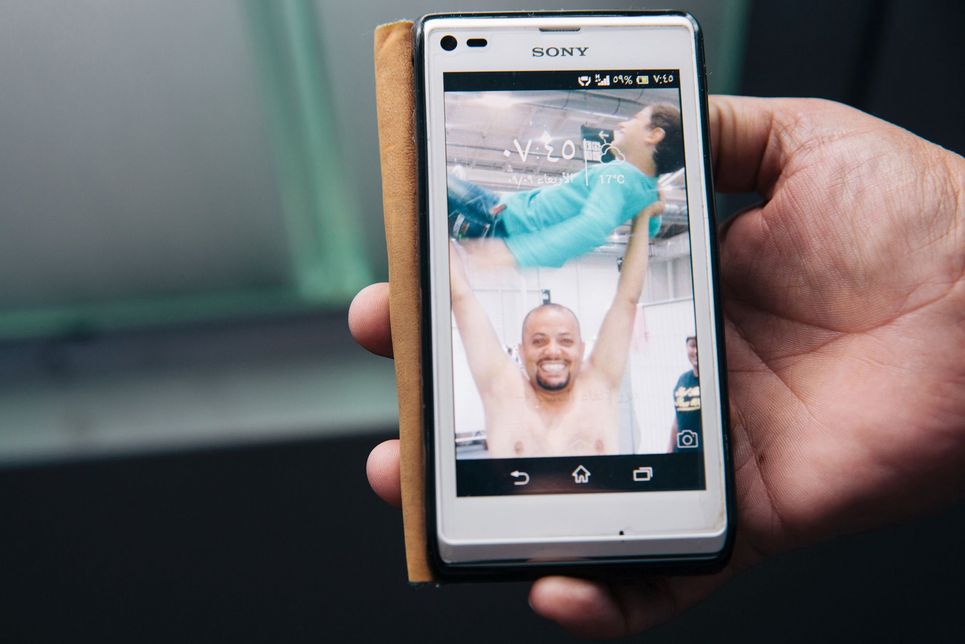 Foto auf einem Handydisplay, auf dem ein Mann mit freiem Oberkörper einen Jungen in die Luft wirft.