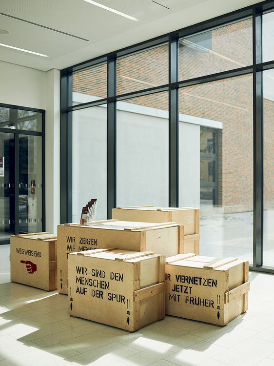 Holzkisten im Museum. Eine der Kisten trägt die Aufschrift:"Wir sind den Menschen auf der Spur."