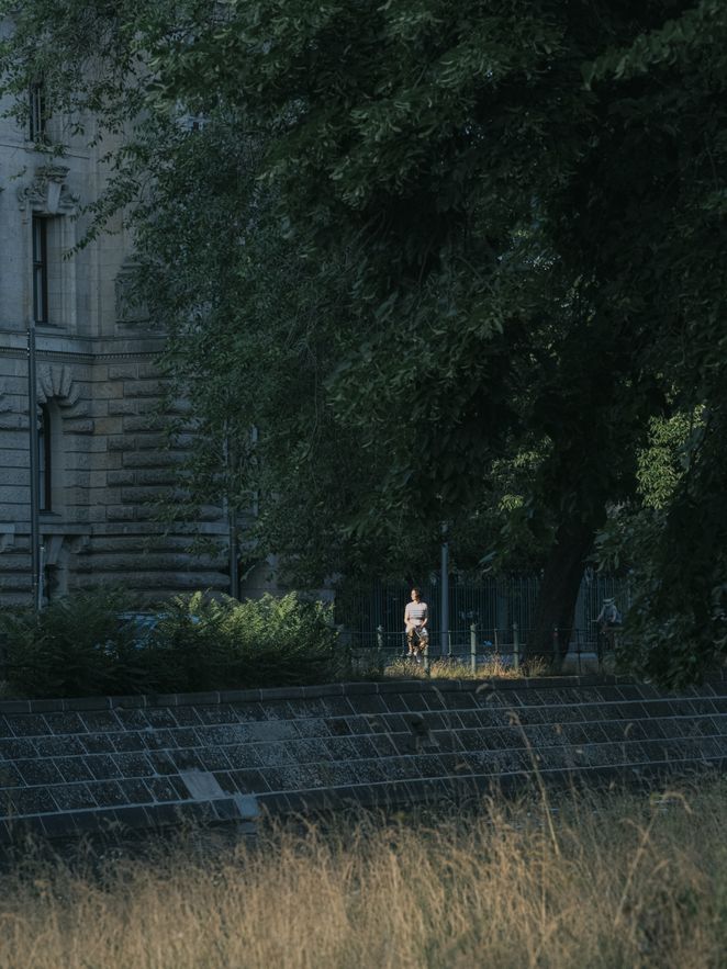 Jutta Allmendinger sitzt in der Ferne auf einem Zaun in der Natur vor dem WZB.